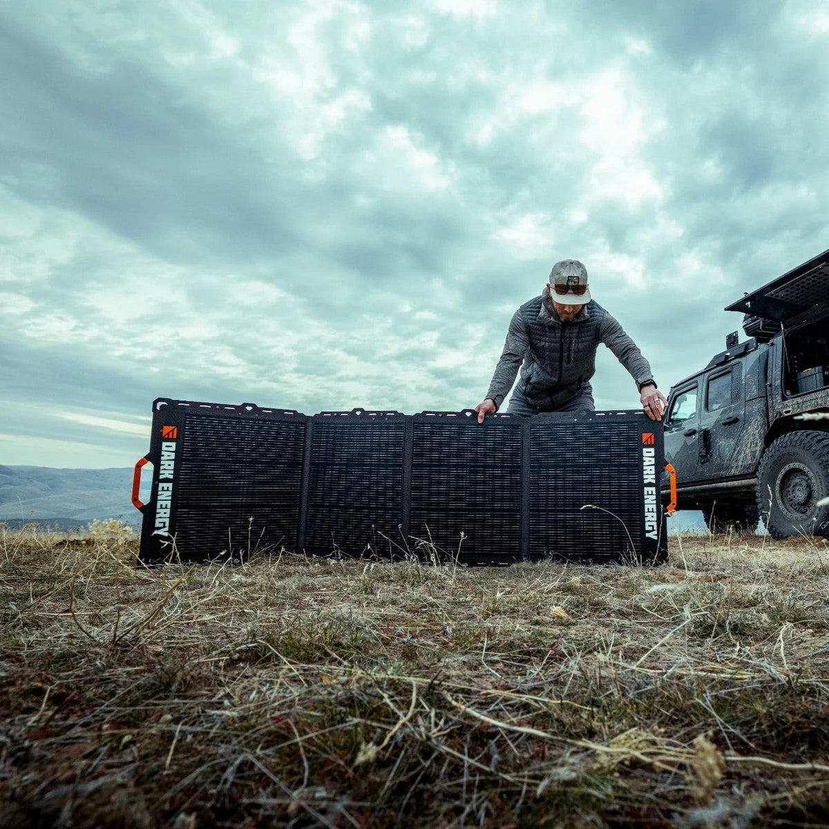 Person setting up a large black mat with 'Dark Energy' branding in an open field.