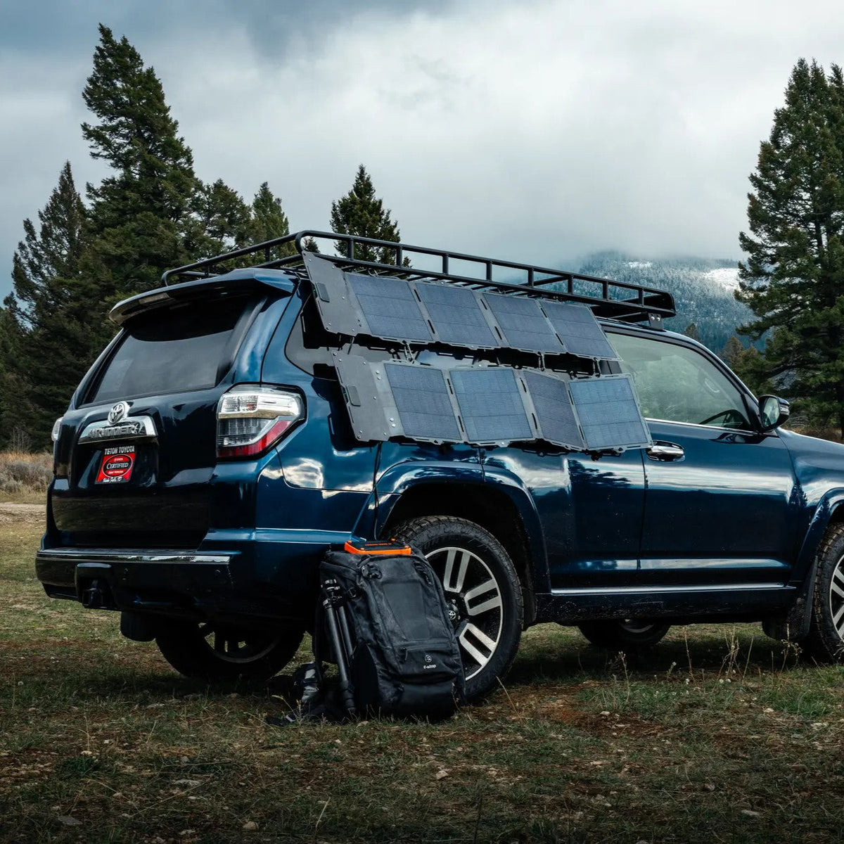 Blue SUV with solar panels on a grassy field with trees and mountains in the background