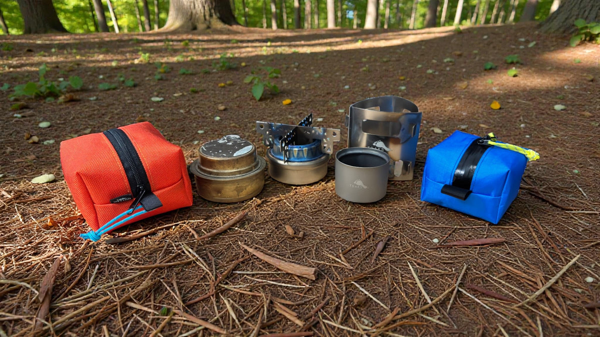 Collection of camping cookware and accessories on a forest floor