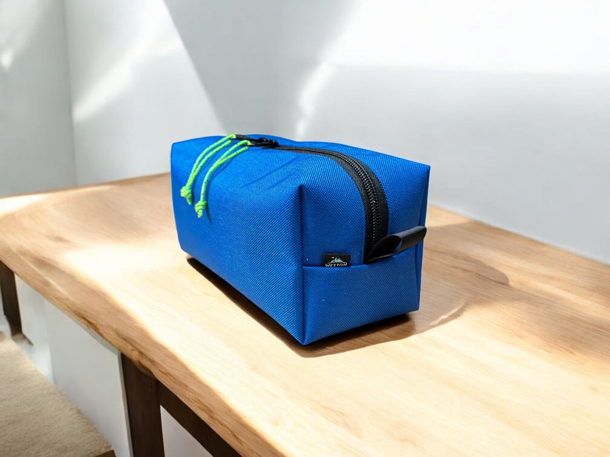 Blue toiletry bag with a black zipper and green pull tab on a wooden surface.
