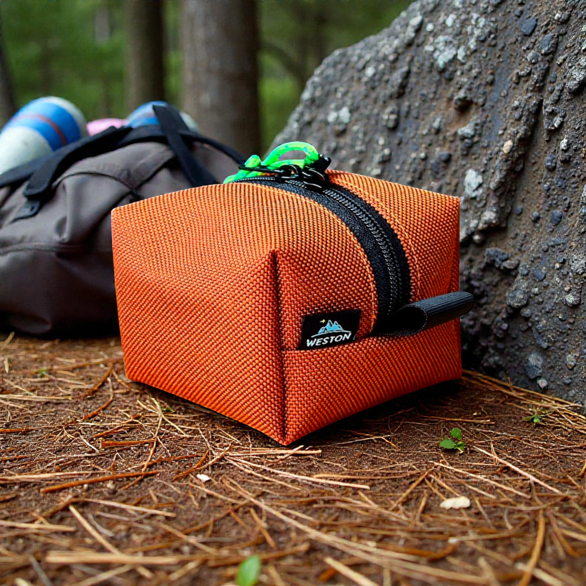 Orange pouch with a black zipper on a forest floor, featuring the Weston brand.