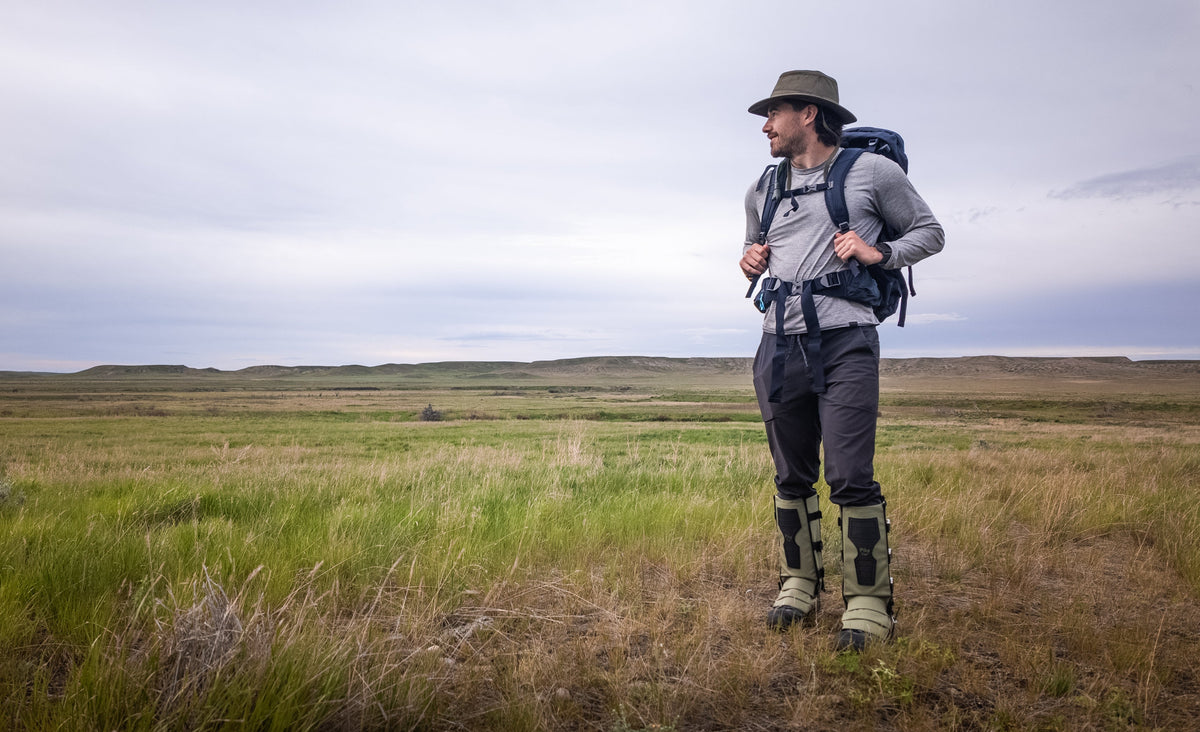 Person hiking in a grassy field wearing outdoor gear