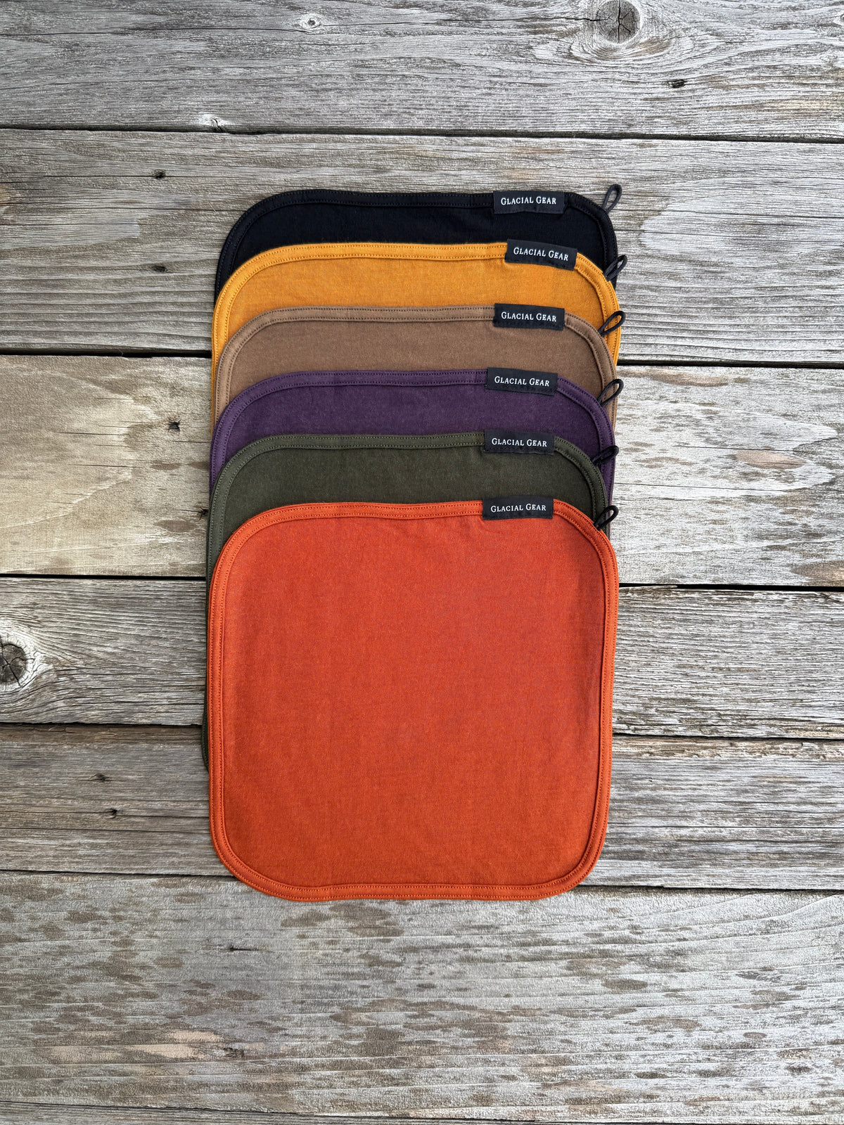 Set of five fabric pouches in different colors arranged on a wooden surface.