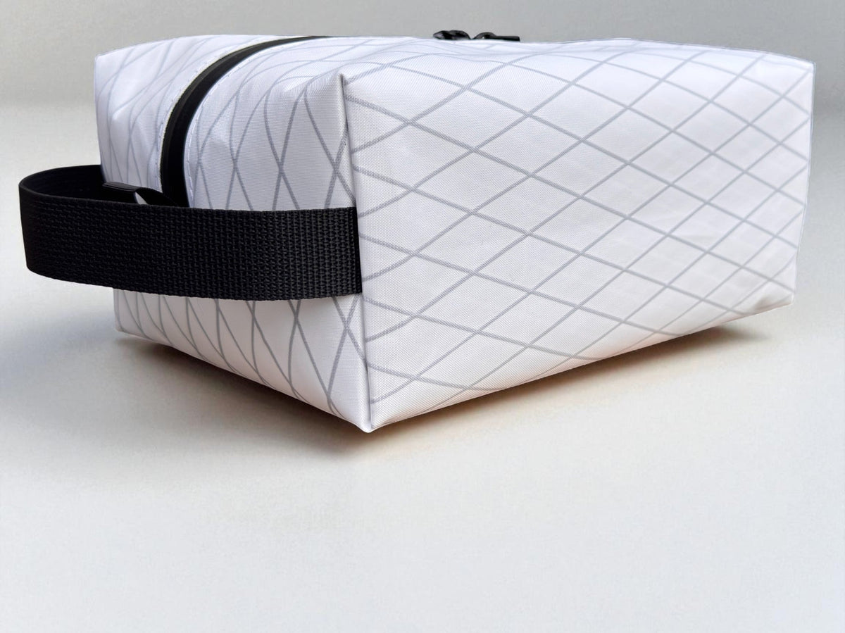 White quilted toiletry bag with black strap on a light gray background