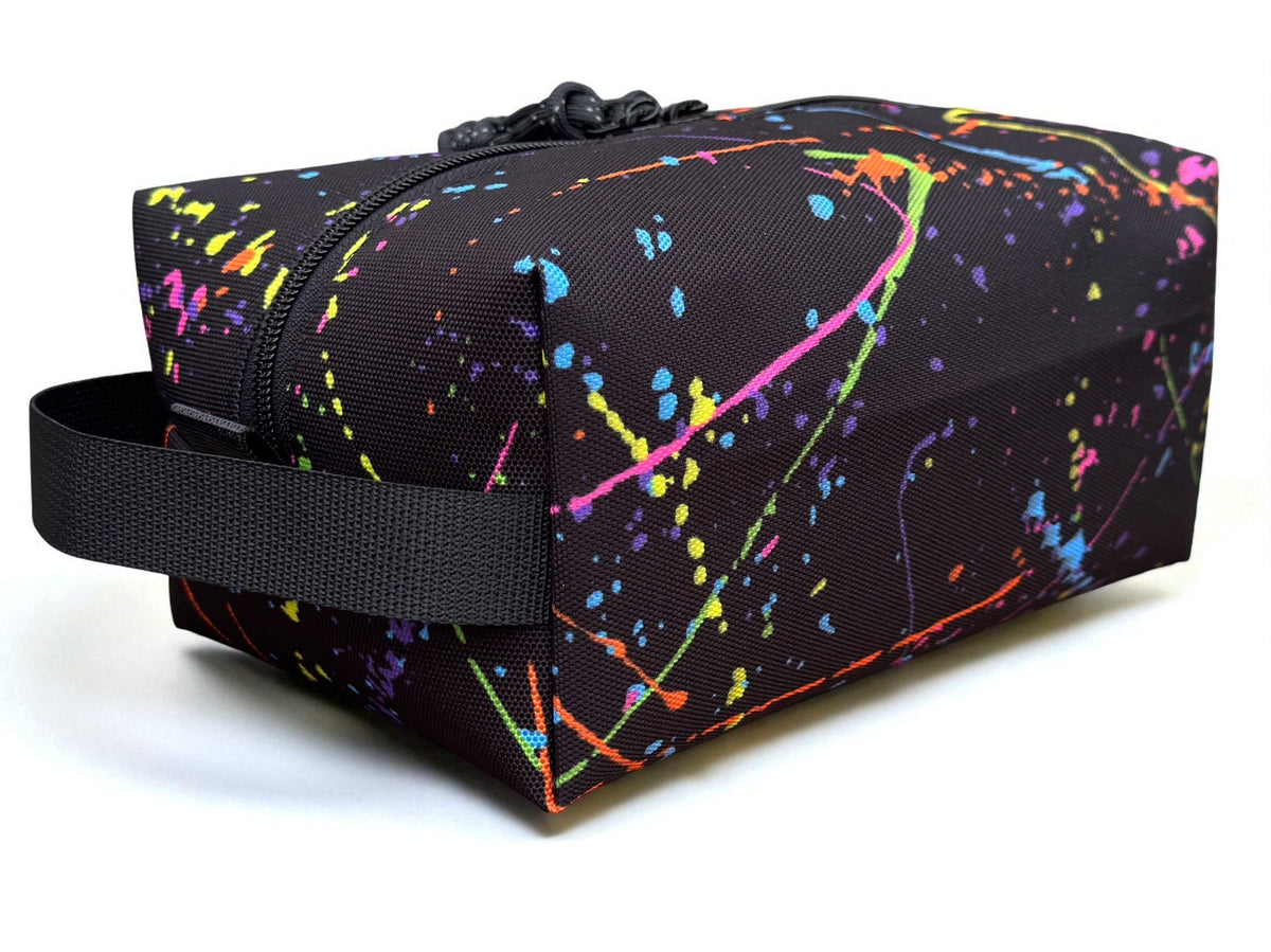 Multicolored splatter-patterned bag with a black strap on a white background