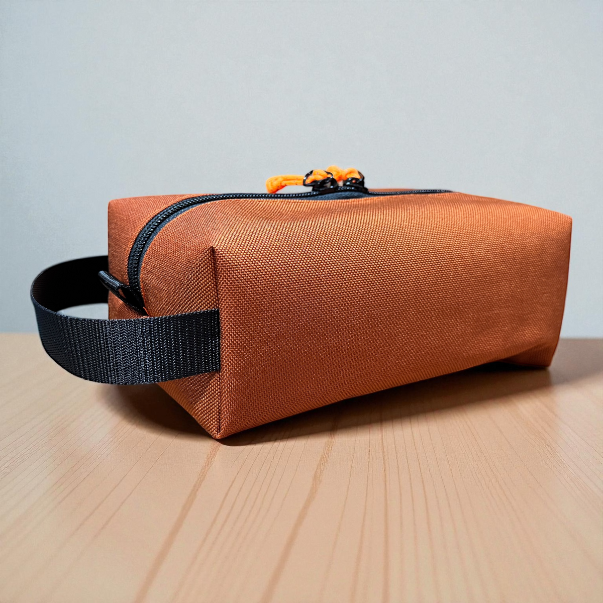 Brown rectangular bag with black strap on a wooden surface and gray background