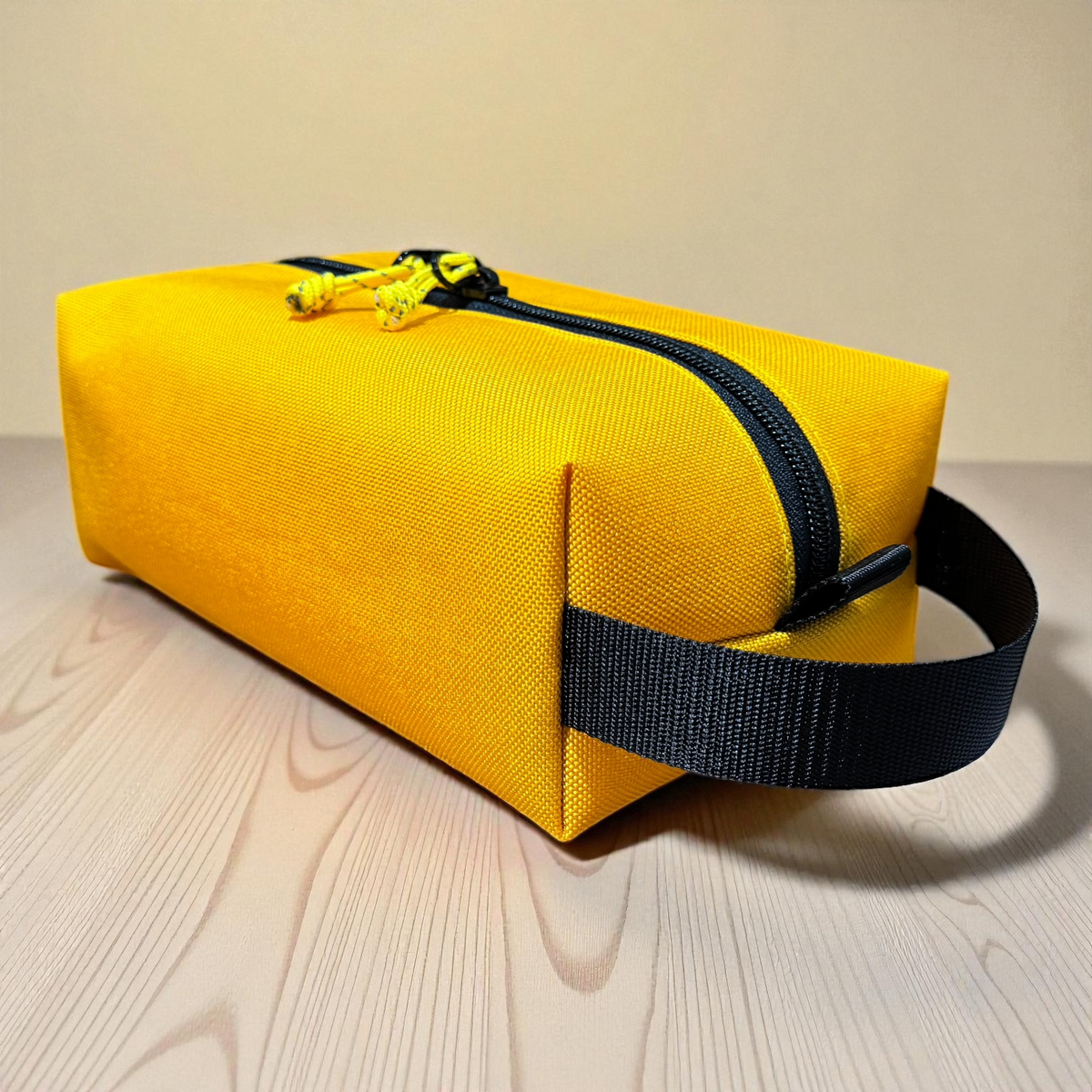 Yellow toiletry bag with black strap on a light wooden surface