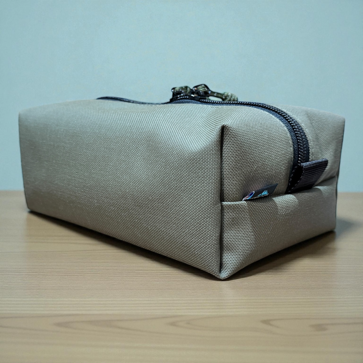 Beige toiletry bag with a zipper on a wooden surface and light blue background