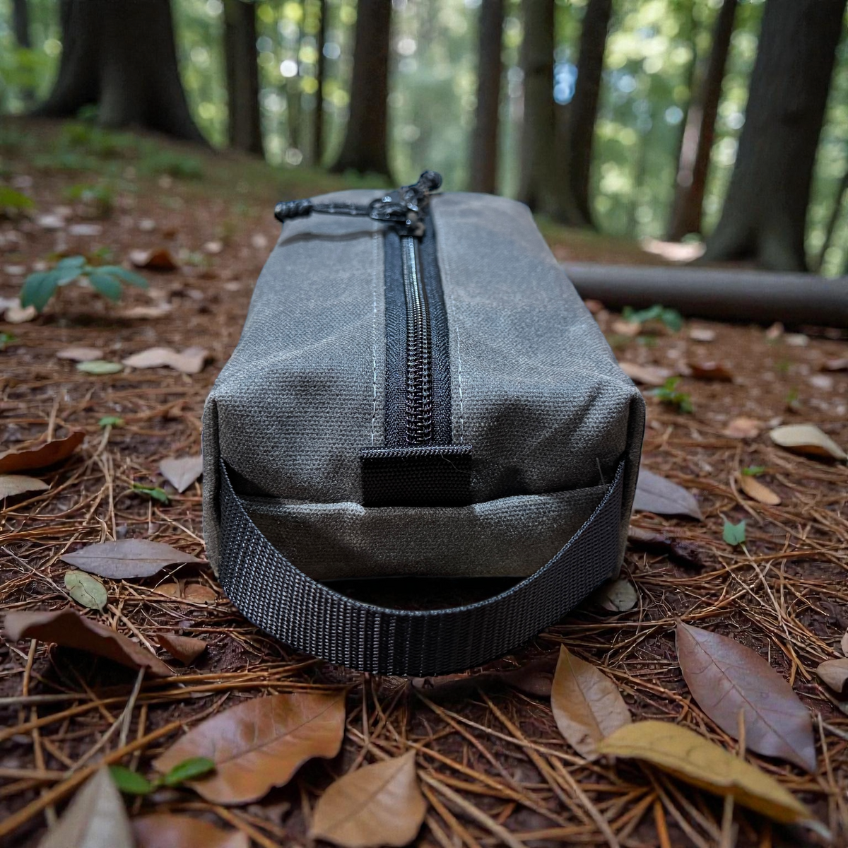 Gray zippered pouch on a forest floor with trees in the background