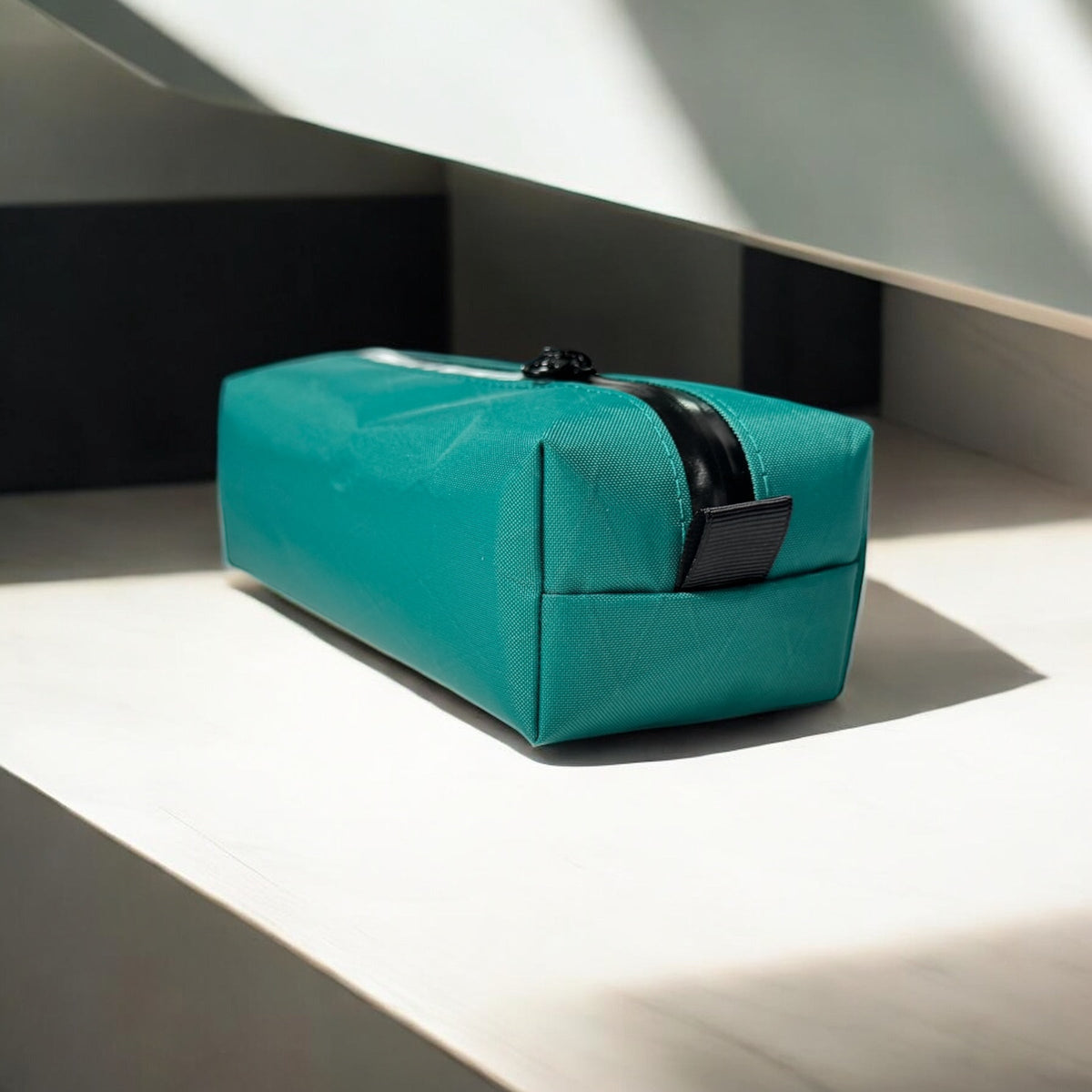Turquoise rectangular pouch with black strap on a light surface