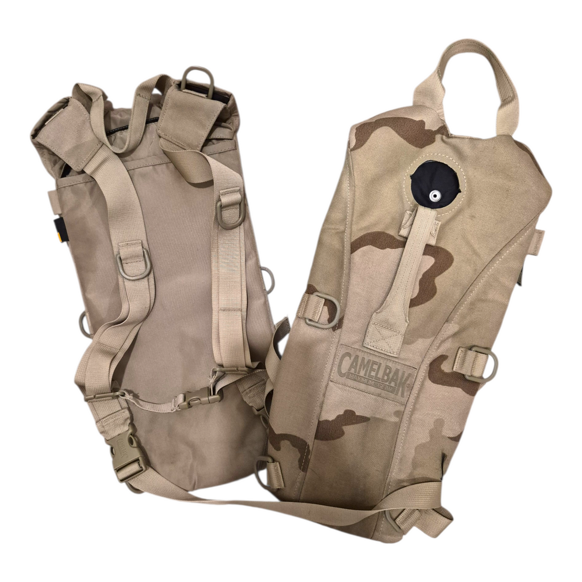 Two CamelBak hydration packs in desert camouflage and solid tan, displayed from front and back angles against a white background.